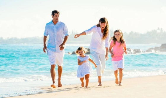 Roditelji s dvije djevojčice hodaju uz more na pješčanoj plaži